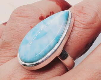 May include: A silver ring with a teardrop-shaped blue and white gemstone. The ring is on a finger.