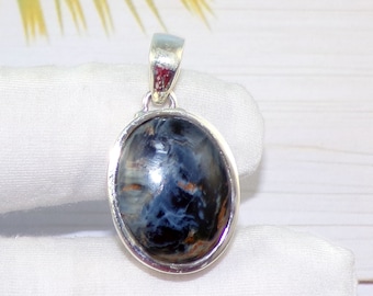 Puede incluir: Colgante ovalado con una piedra preciosa azul oscuro pulida que presenta patrones arremolinados de azul claro y marrón. La piedra está engastada en un marco de metal plateado con una fianza a juego para una cadena de collar.