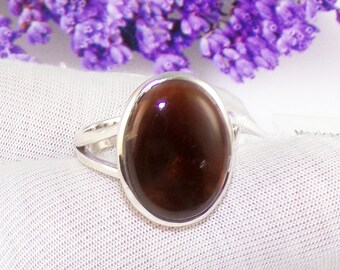May include: A silver ring with a dark brown oval gemstone. The ring is set on a white fabric background.