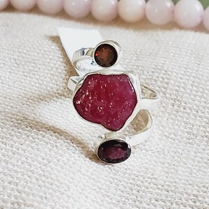 Peut inclure: Une bague en argent avec trois pierres pr&eacute;cieuses rouges. La plus grande pierre est de forme irr&eacute;guli&egrave;re et brute, tandis que les deux plus petites pierres sont rondes. La bague est con&ccedil;ue pour &ecirc;tre port&eacute;e au majeur.
