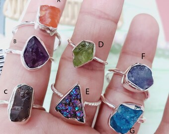 Peut inclure: Sept bagues en argent avec des pierres précieuses de différentes couleurs. Les bagues sont étiquetées de A à G. Les pierres précieuses sont orange, violette, marron, irisée, verte, bleue et bleu clair.
