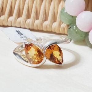 May include: A silver ring featuring two pear-shaped citrine gemstones. The ring has a simple, contemporary design.