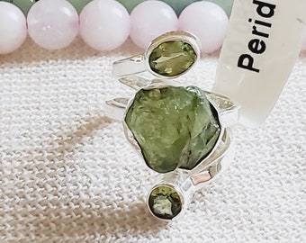 Peut inclure: Une bague en argent avec trois pierres de péridot vertes. La plus grande pierre est un péridot brut et naturel. La bague est étiquetée "Péridot".