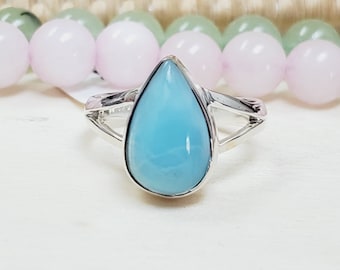May include: A teardrop-shaped ring with a light blue gemstone set in a silver band.