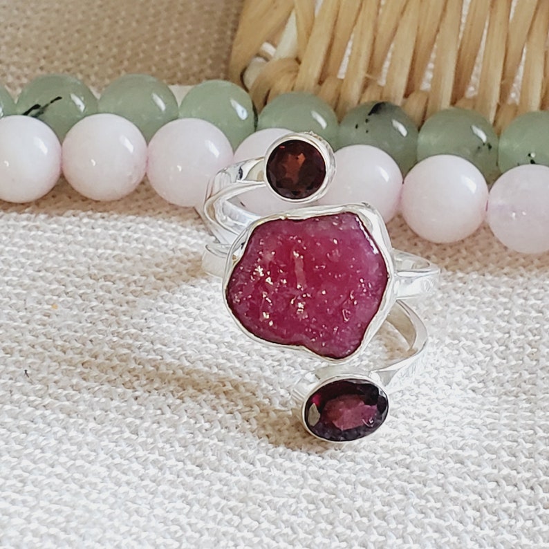 Peut inclure: Une bague en argent avec une grande pierre pr&eacute;cieuse rose brute et deux petites pierres rondes de couleur grenat.