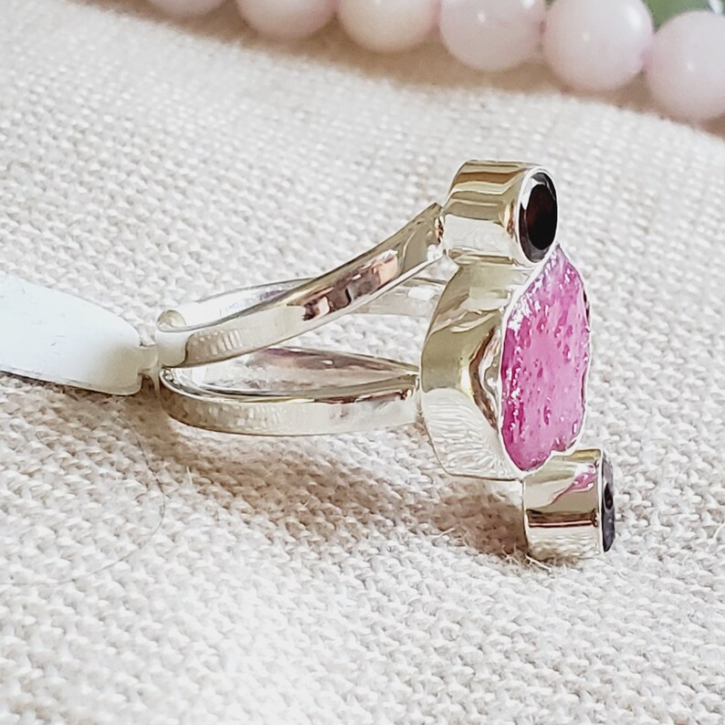 Peut inclure: Une bague en argent avec un sertissage de pierres pr&eacute;cieuses roses et noires. La bague a une double bande et les pierres sont serties en grappe.