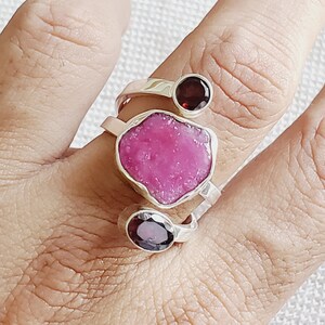 Peut inclure: Une bague en argent avec trois pierres pr&eacute;cieuses. La plus grande pierre est rose et de forme irr&eacute;guli&egrave;re. Les deux plus petites pierres sont rondes et rouges.
