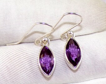 May include: A pair of silver earrings featuring purple amethyst gemstones. The earrings have a simple design with a small, round bead at the top and a marquise-shaped gemstone hanging below.