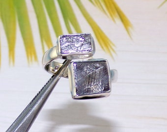 Peut inclure: Une bague en argent avec deux incrustations carrées de météorite. Les incrustations ont une surface texturée unique.