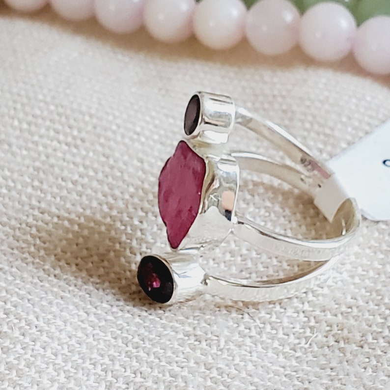 Peut inclure: Une bague en argent avec trois pierres pr&eacute;cieuses rouges. La bague a une double bande et les pierres pr&eacute;cieuses sont serties dans l'argent.