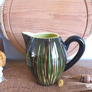 May include: A green and brown ceramic jug with a yellow rim and a black handle. The jug has a striped pattern.