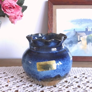 May include: A blue and brown ceramic vase with a ruffled rim. The vase has a gold label that reads "Gres La Borne, France".