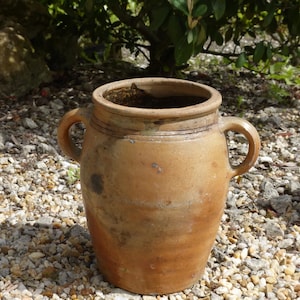 May include: A large, brown, earthenware crock with two handles. The crock is sitting on a bed of small, white stones.