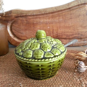 May include: Green ceramic sugar bowl with a lid shaped like a basket of fruit. The bowl has a woven basket design and is decorated with green fruit.