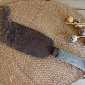 May include: A rusty, old, hand-forged, metal,  garden tool with a wooden handle. The tool is lying on a woven, straw mat.