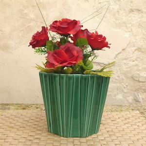 Puede incluir: Una maceta de cerámica verde con diseño acanalado, llena de un ramo de rosas rojas.