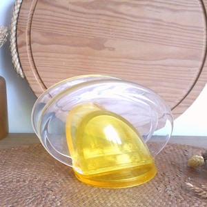 May include: A clear glass napkin holder with a yellow plastic insert. The holder is designed to hold napkins upright.