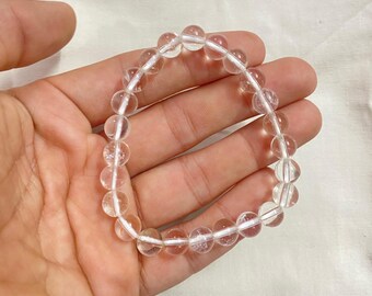May include: A clear quartz crystal beaded bracelet with a simple design. The bracelet is made of round beads and is strung on a clear elastic cord.