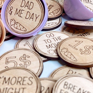 May include: Wooden tokens with various phrases and images, including "Dad & Me Day", "Go For A Hike", "Go To The Movies", "5$", "S'mores Night", and "Breakfast For Dinner".