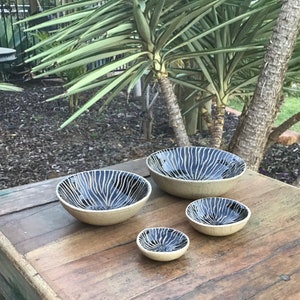May include: Four ceramic bowls with black and white striped patterns. The bowls are arranged in a size order from largest to smallest on a wooden surface.