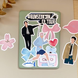 Può includere: Una collezione di adesivi con illustrazioni di una persona, fiocchi, un cuore e un'audiocassetta. Gli adesivi sono in vari colori, tra cui rosa, blu e nero. Il testo sugli adesivi include "#RUNSEOKJIN EP TOUR" e "DON'T LOVE ME".