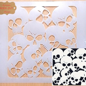 May include: A white laser-cut mylar stencil with a repeating skull design. The stencil is on a wooden surface, with a small inset image of the skull design. The text "Durable Laser Cut Mylar" is visible.
