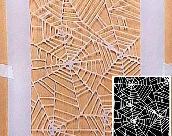 May include: A rectangular stencil featuring a repeating spider web pattern with intricate cutouts. The semi-transparent material is labeled with the text Durable LASER CUT Mylar. An inset shows the pattern in high-contrast black and white.