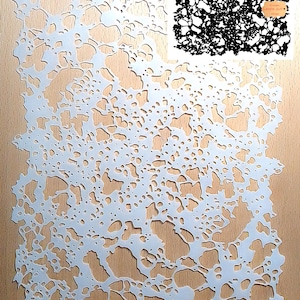 Peut inclure: Pochoir en vinyle blanc avec un motif délicat et complexe de petits et grands cercles et de formes organiques. Le pochoir est posé sur une surface en bois brun clair. Le texte "Laser Cut" est visible sur une petite étiquette blanche.