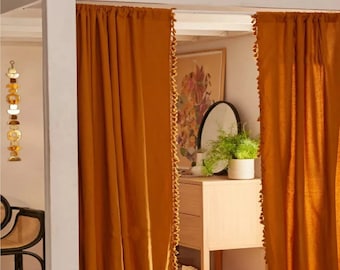 May include: A pair of mustard yellow curtains with a tassel trim. The curtains are hung on a white rod and are partially drawn, revealing a room with a wooden dresser and a potted plant.