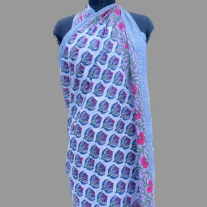 Puede incluir: Un pareo blanco con un estampado floral repetido en azul, morado y rosa. El pareo est&aacute; drapeado sobre un maniqu&iacute;. El borde presenta un dise&ntilde;o a rayas en azul y blanco, con detalles florales en rosa y verde.
