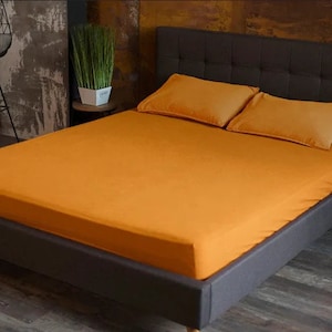 May include: A dark grey upholstered bed frame with a tufted headboard and a mustard yellow fitted sheet. The bed is made with two matching pillowcases.