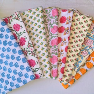 Puede incluir: Una colección de ocho colchas de algodón con varios patrones florales y geométricos en tonos de azul, rosa, amarillo y naranja. Las colchas están dobladas y dispuestas en forma de abanico.