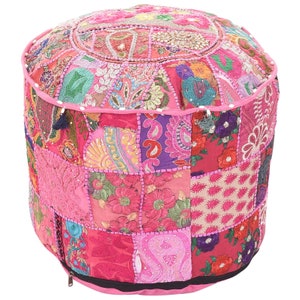 May include: A pink and multi-coloured patchwork pouffe ottoman with a zipper closure. The pouffe is made of various fabrics with embroidery and sequins.