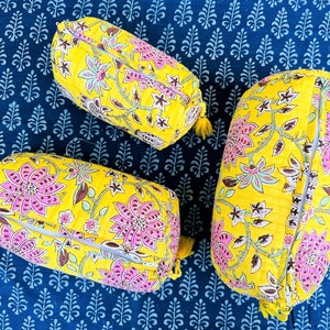 May include: Three yellow fabric cylindrical pillows with pink and green floral patterns. The pillows are on a blue patterned fabric background.