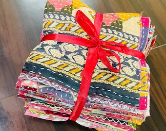 May include: A stack of colorful fabric squares, likely for quilting or crafting, is tied with a bright red ribbon. The fabric features a variety of patterns and colors, including floral and geometric designs. The edges of the squares are visible, showing the layered construction.