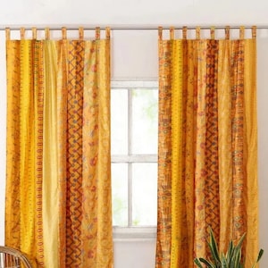 Può includere: Un paio di tende a motivi gialli e arancioni con un design patchwork. Le tende sono appese a un'asta bianca e sono realizzate in un tessuto morbido e fluido.
