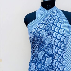 Puede incluir: Un pareo estampado en azul y blanco drapeado sobre un maniqu&iacute;. La tela presenta dise&ntilde;os florales y geom&eacute;tricos. El pareo es de color azul oscuro con detalles en blanco y un borde a rayas.