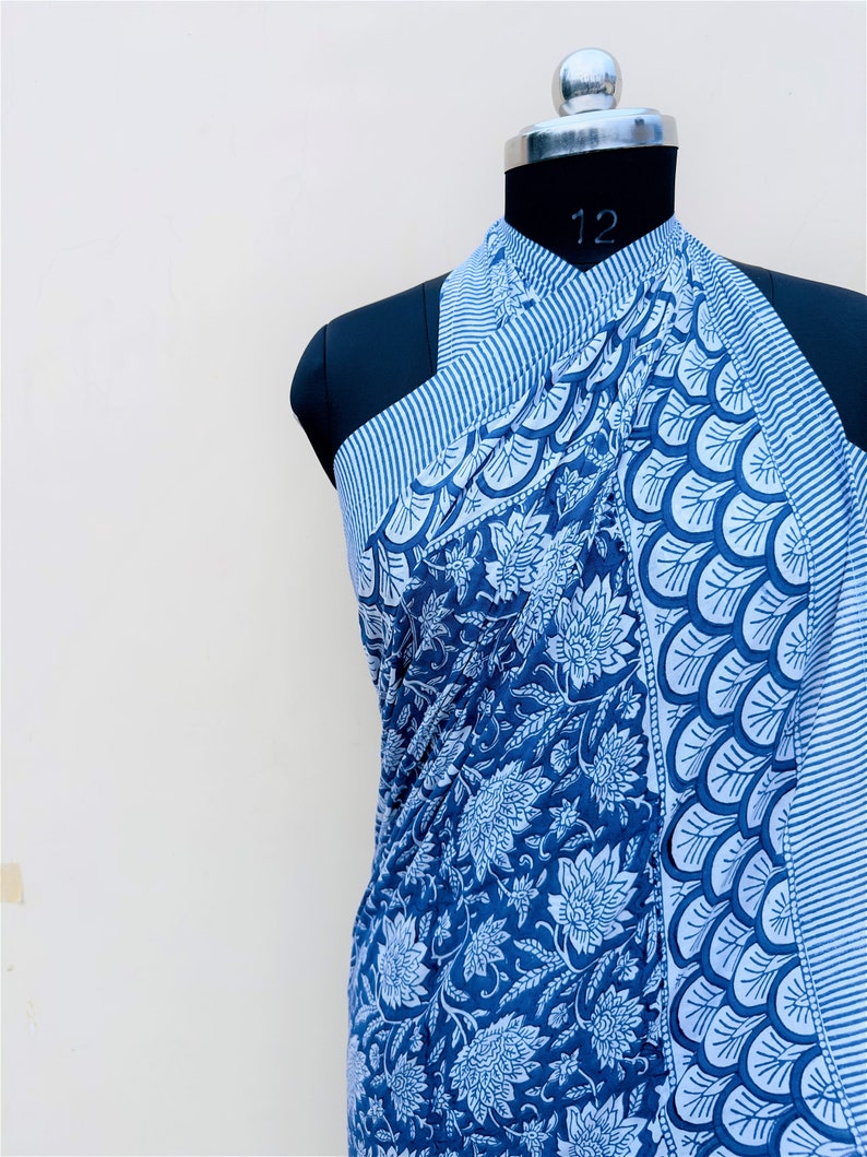 Puede incluir: Un pareo estampado en azul y blanco drapeado sobre un maniqu&iacute;. La tela presenta dise&ntilde;os florales y geom&eacute;tricos. El pareo es de color azul oscuro con detalles en blanco y un borde a rayas.