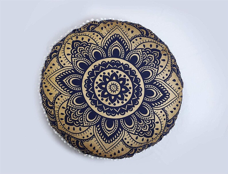 May include: Round decorative cushion with a gold and navy blue mandala design. The cushion has a white pom-pom trim around the edge. The cushion is a decorative item.
