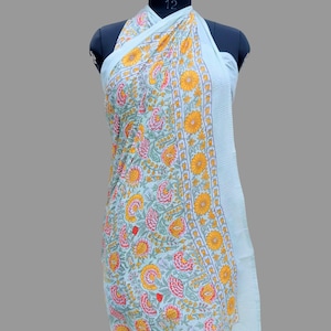 Puede incluir: Un pareo verde claro con un estampado floral de flores amarillas y rosas y hojas verdes. El pareo est&aacute; drapeado sobre un maniqu&iacute; y tiene un borde a rayas.