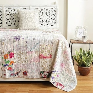 Puede incluir: Colcha blanca kantha con bordado floral de colores sobre una cama con cabecero tallado en blanco. La colcha está hecha de tela de patchwork y tiene un aspecto desgastado.
