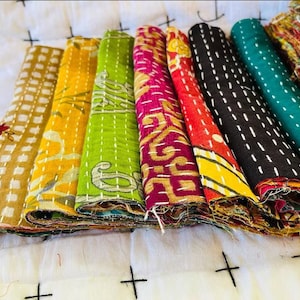 Peut inclure: Une pile de huit chutes de tissu kantha colorées, chacune avec un motif et des points différents. Les tissus sont pliés et disposés en rangée, avec le tissu le plus coloré en haut.