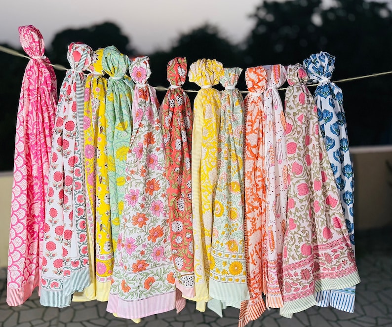 May include: A collection of colourful cotton scarves with floral patterns. The scarves are hanging on a clothesline and are arranged in a row. The scarves are all different colours and patterns, but they all have a similar floral design.