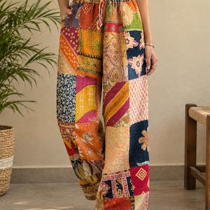 Könnte beinhalten: Weit geschnittene Hose mit einem lebendigen Patchwork-Design aus verschiedenen Blumen-, geometrischen und Paisley-Mustern in Rot-, Gelb-, Orange-, Blau- und Grüntönen. Die Hose hat einen elastischen Bund mit Kordelzug und seitliche Taschen.