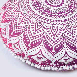 May include: Round floor cushion with a mandala design in shades of purple and white. The cushion has a gradient effect, transitioning from pink to purple. White pom-poms trim the edge. A decorative accent for home decor.
