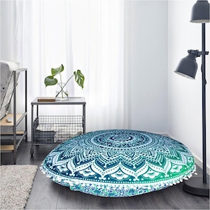 May include: Round floor cushion with a mandala design in shades of teal and white. The cushion has a gradient effect, transitioning from dark teal to light green. White tassels trim the edge. The cushion is approximately 40 inches in diameter.