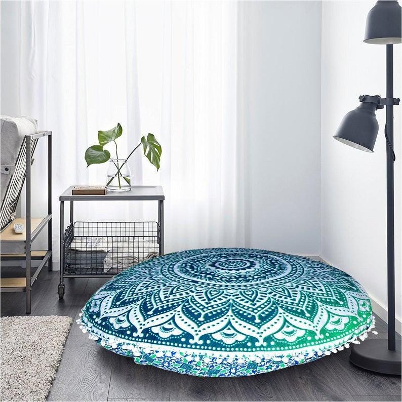 May include: Round floor cushion with a mandala design in shades of teal and white. The cushion has a gradient effect, transitioning from dark teal to light green. White tassels trim the edge. The cushion is approximately 40 inches in diameter.