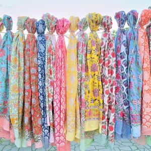 Puede incluir: Una colecci&oacute;n de coloridas bufandas con estampados florales colgadas de un tendedero. Las bufandas presentan varios dise&ntilde;os en tonos de rosa, azul, amarillo y verde. Cada bufanda est&aacute; anudada en la parte superior, mostrando los vibrantes patrones y colores.