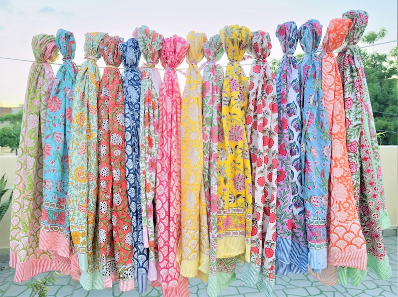 Puede incluir: Una colecci&oacute;n de coloridas bufandas con estampados florales colgadas de un tendedero. Las bufandas presentan varios dise&ntilde;os en tonos de rosa, azul, amarillo y verde. Cada bufanda est&aacute; anudada en la parte superior, mostrando los vibrantes patrones y colores.