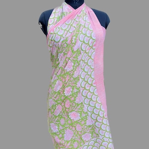 Puede incluir: Un pareo con estampado floral verde y rosa exhibido en un maniqu&iacute;. El pareo presenta un gran estampado floral en un lado y un borde a rayas en el otro. La tela est&aacute; drapeada para mostrar el dise&ntilde;o.